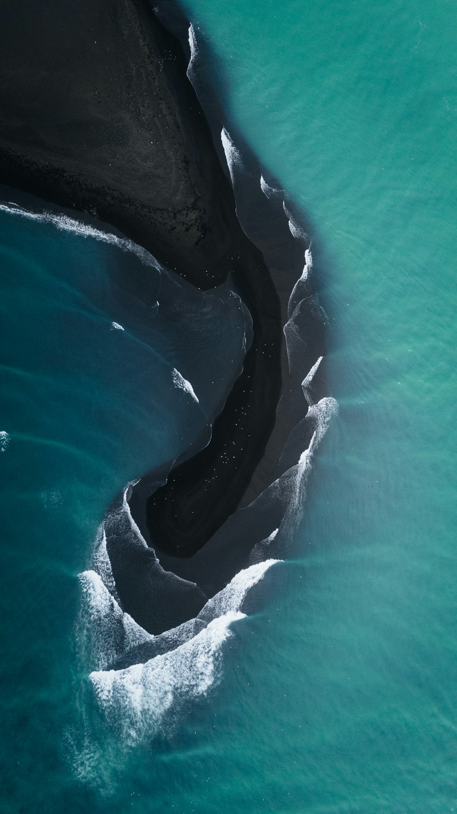 An aerial photograph of turquoise waves meeting a black sand beach in Iceland